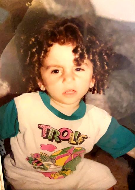 Tomer as a small child with curly hair, in a T-shirt with the word Trolls.